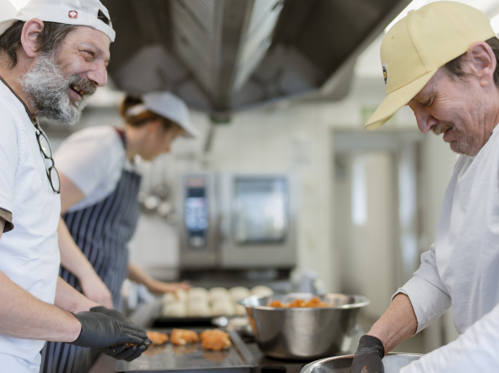 Eine Gruppe von Bewohnenden unterhält sich lachend in der Küche, während sie gemeinsam das Mittagessen zubereiten.